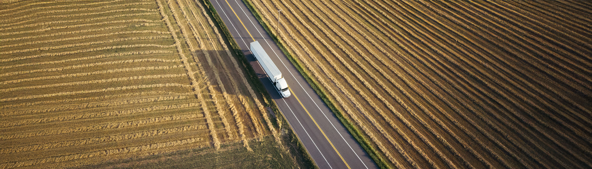 Aerial view of white semi trailer on highway surrounded by farmland
