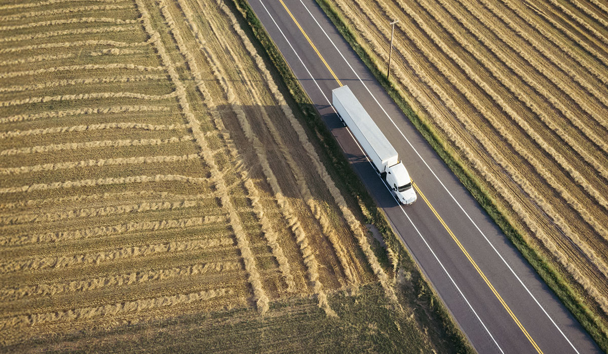 Aerial view of white semi trailer on highway surrounded by farmland