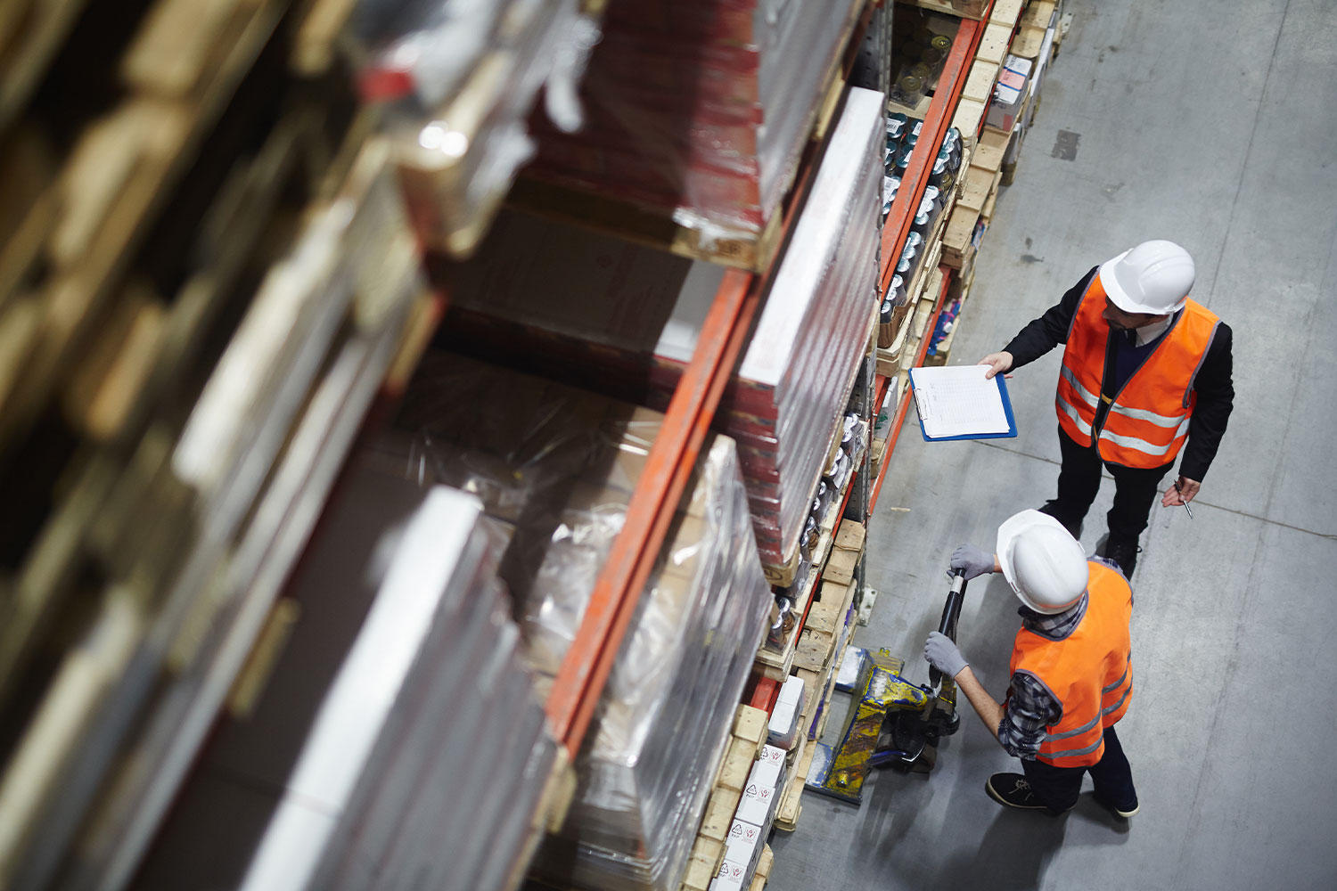 Logistics-Consulting-02 Overhead view of two workers in orange vests and hard hats in a warehouse