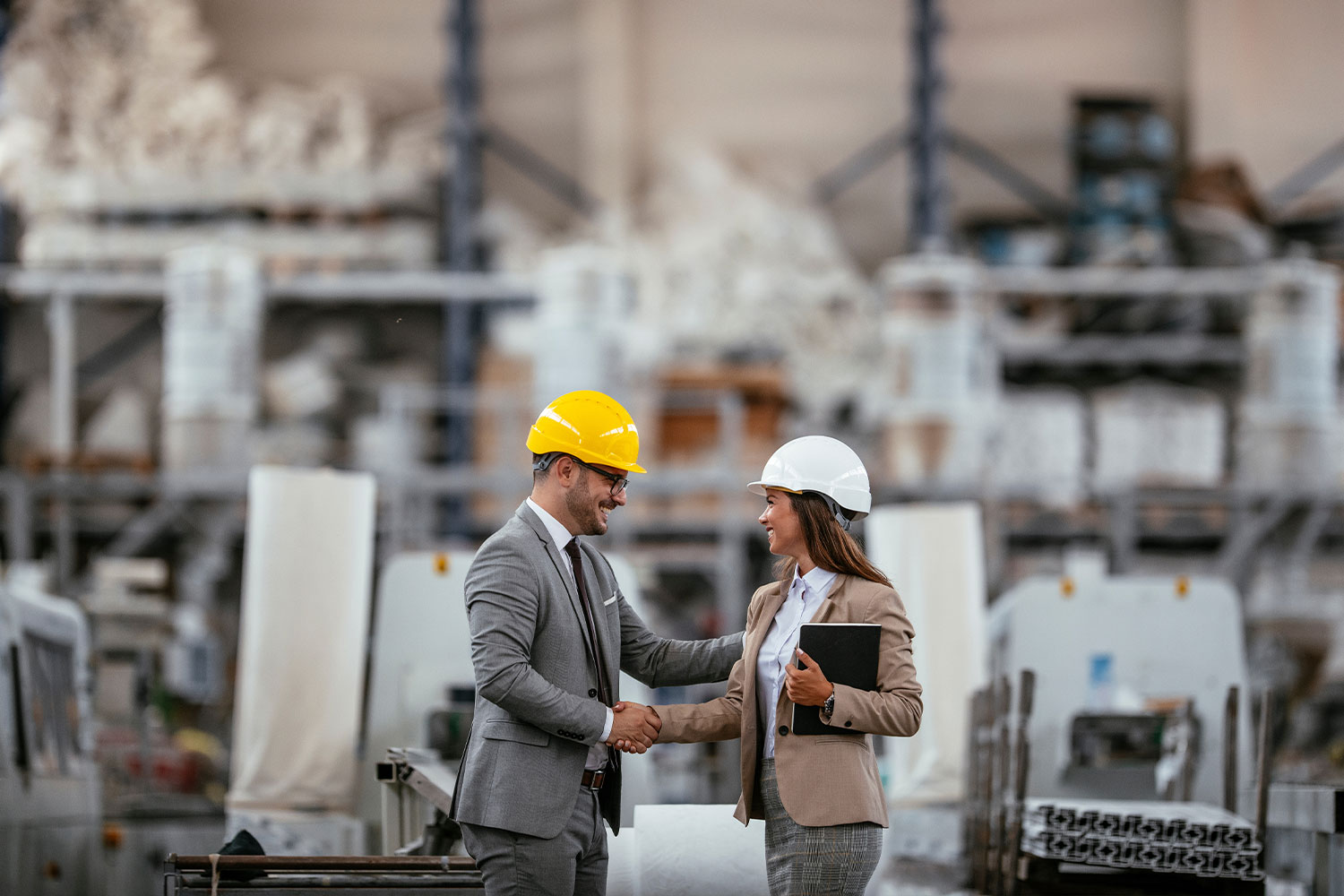 Logistics-Consulting-05 Man and woman in hard hats shaking hands in warehouse.