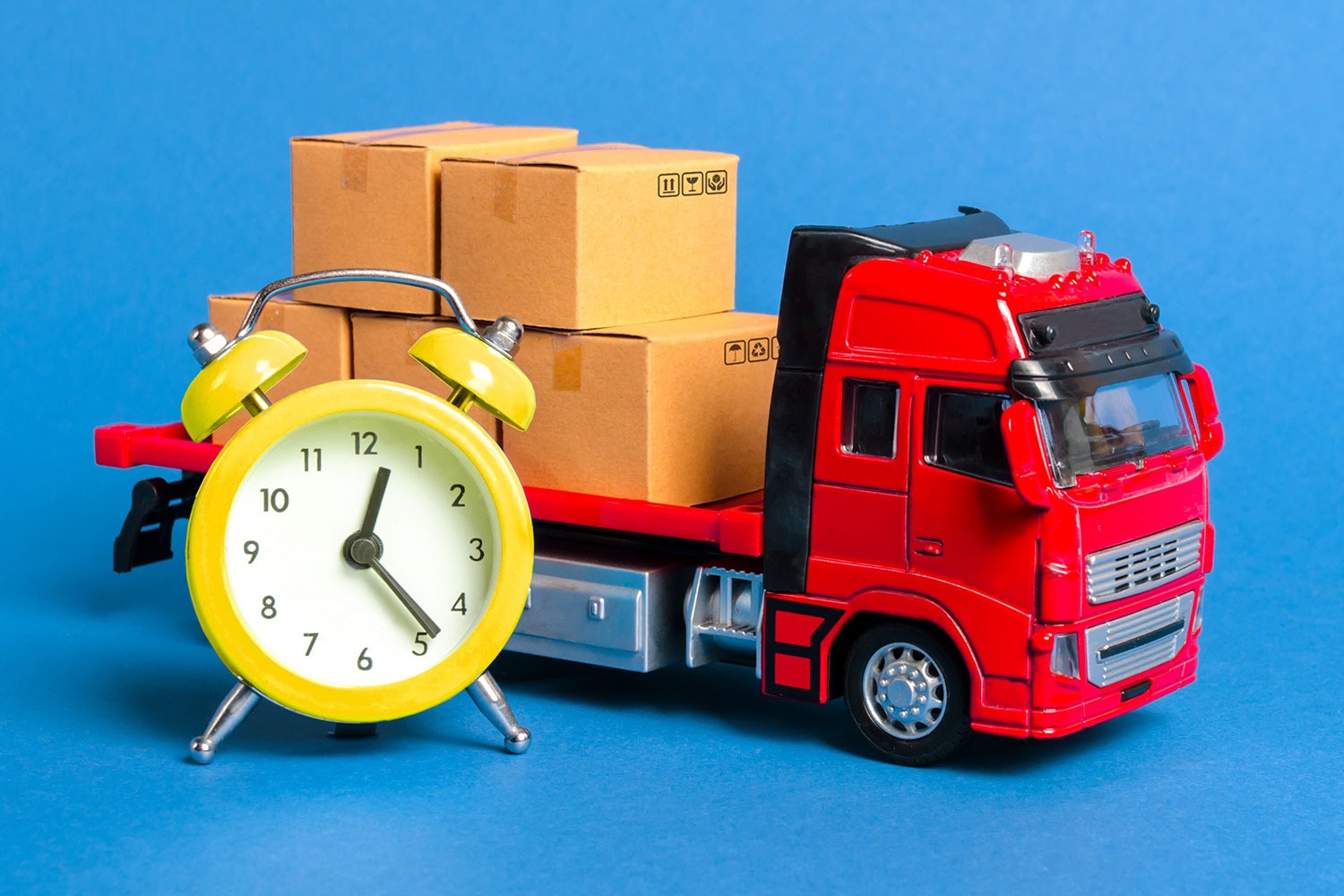 Rental-04 Red toy flatbed truck with boxes on the back sitting next to an alarm clock.